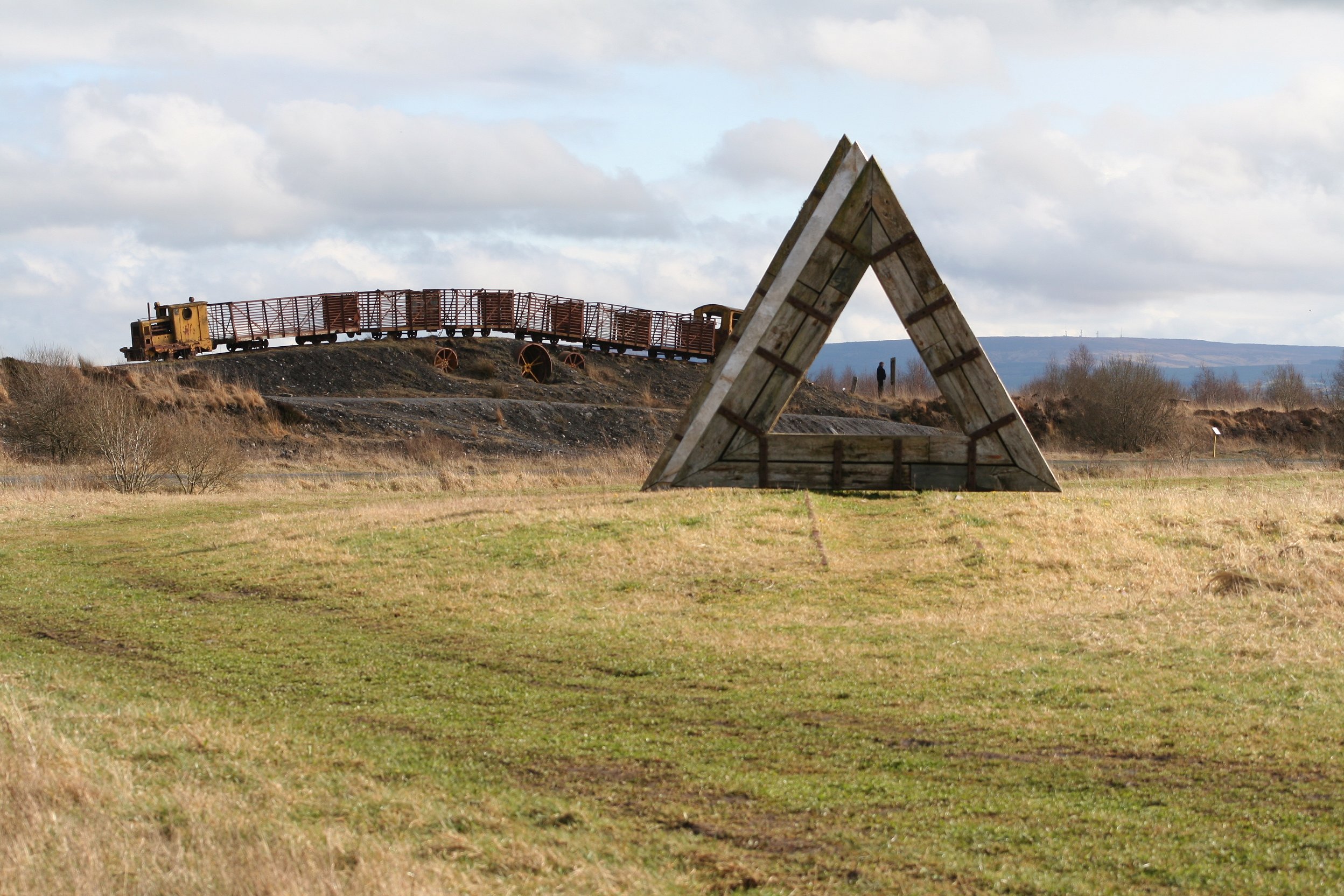 Sculptures at Lough Boora: a tall triangular timber frame and a train of rail wagons on the cutaway bog