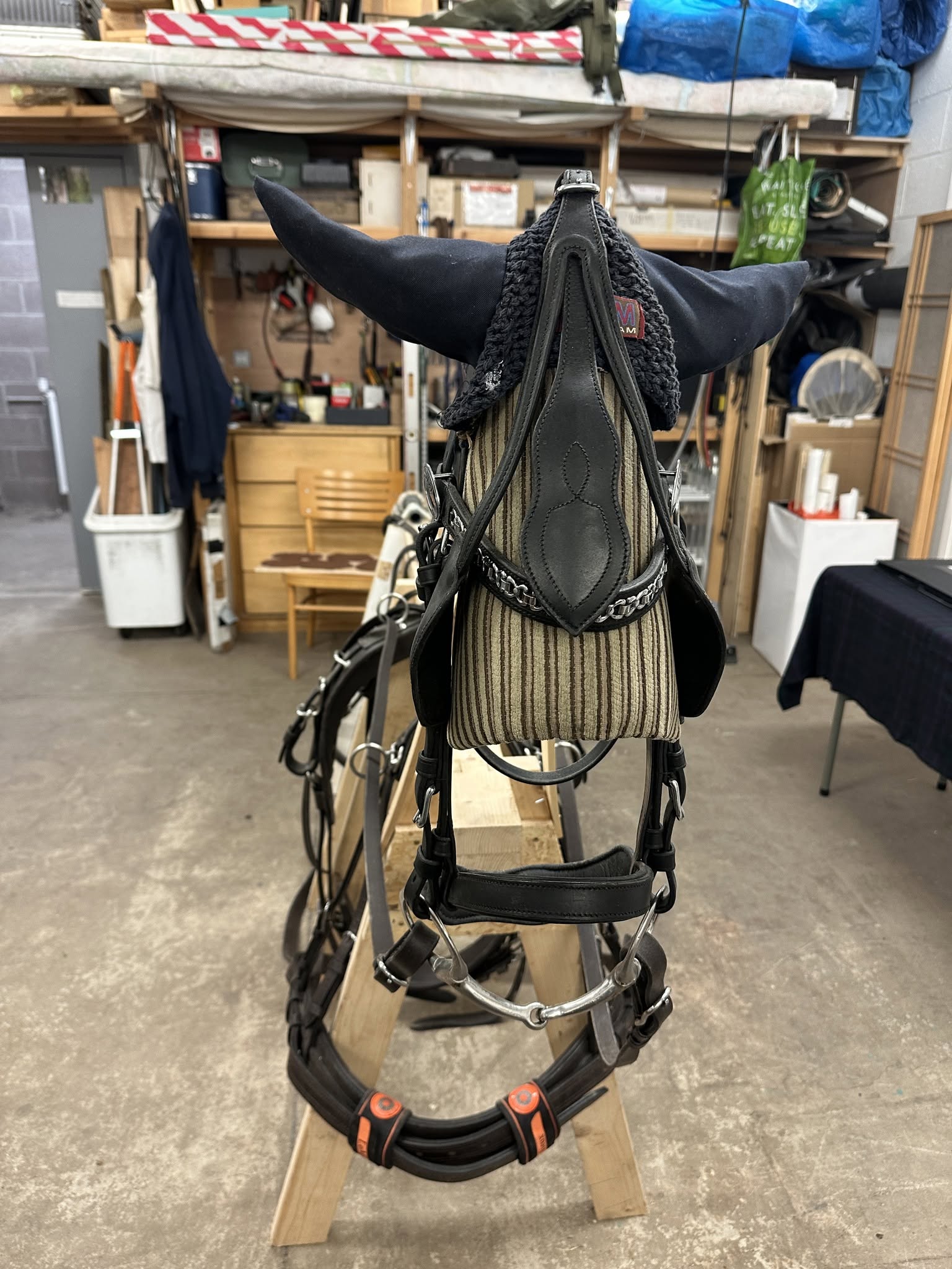 Front view of the harness and bridle on the wooden frame, with a knitted ear bonnet